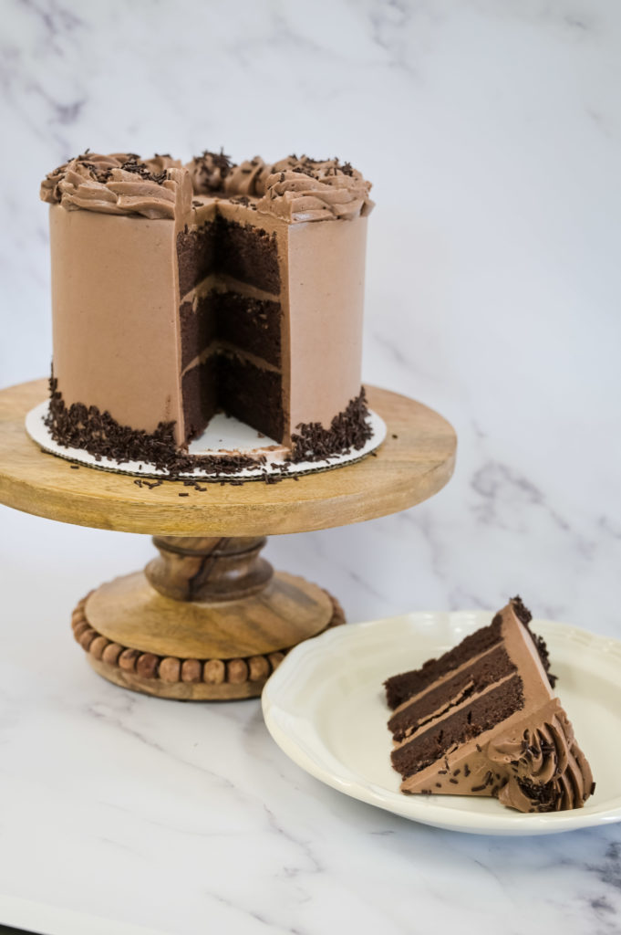 Perfect Chocolate Cake and chocolate buttercream, Three Layers on wooden cake tray with plated slice 